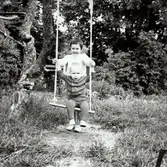 Storasyster Ilse Tobiasson (född 1960, gift Glimberg) gungar lillebror Lars-Åke Jansson (född 1964, gift Dahlén), i Högsbo år 1965. Lars-Åkes farmor Maj hyrde en sommarstuga uppe på berget, väster om Dag Hammarskjöldsleden, mittemot Slottsskogsvallen.