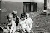 Tre barn sitter på innergården till Krokslättsgatan 3 år 1963. Från vänster: Kenneth Sjögren (1960 – 2017), kusinen Ilse Tobiasson (född 1960, gift Glimberg) samt deras kompis Jörgen Larsson (född 1958). Till höger ses Ilses dockvagn. Ilse och Jörgen var grannar på Krokslättsgatan 3 i Mölndal. Tvättstugan fanns där fönstrena ses i bakgrunden. På innergården brukade kvinnor träffas för att fika och bland annat knyta ryamattor. På den tiden var gårdarna uppdelade med flertalet staket (ses till höger). Mellan vissa gårdar fanns en låst grind som gjorde att man behövde gå runt byggnaden för att besöka andra i samma område. Vicevärden (Ella Johansson) hade nyckel till grinden. Barnen fick enbart leka på den inhägnade delen som tillhörde adressen. På varje gård fanns flertalet soptunnor, där råttor höll till.