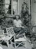 Midsommar 1940. Mary Ekdahl (1920 - 1988, gift Ekman) sitter och poserar på trädgårdsmöblerna utanför föräldrarhemmet i Kålltorp. Hon gifte sig senare med Björn Ekman och paret bosatte sig i Kållered. Relaterat motiv: A2856.