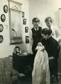 Manne Ekmans (född 1955) dopdag hos Rothwalls, där familjen bodde. Stående från vänster: bröderna Ulf-Göran och Svante Ekman. Sittande: Mary Ekman (1920 - 1988) hållandes sonen Manne i sitt knä. På väggen till vänster ses fadern Björn Ekmans avfotograferade släktingar.