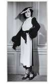 Mannekäng visar svartvit kappklänning med liten ståkrage, knäppning fram, knytskärp och ärm med pälskant. Liten hatt och remsandaler med vristrem. NK:s Franska damskrädderi våren 1938, möjligen från Jeanne Paquin.