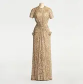 Aftonklänning av skir guldspets med paljett- och pärlbroderi på axlar och höftparti, kort ärm och rynkning mot livet. Beställd från NK:s Franska damskrädderi av Ella Ros född Littorin (1898-1977). Levererad 1941-1942.