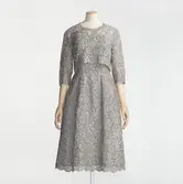 Klänning monterad på docka, av silvergrå gipyrspets med bolero som knäpps bak med spetsklädda knappar. Beställd från NK:s Franska damskrädderi av drottning Louise av Sverige (1889-1965). Troligen buren på prinsessan Alexandas av Storbritannien bröllop i Westminster Abbey, april 1963. Levererad mars 1963. I Livrustkammarens samlingar, LRK_15040.