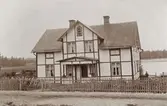 Ett större bostadshus med veranda, på landet. I bakgrunden syns en sjö. Ca 1910.
