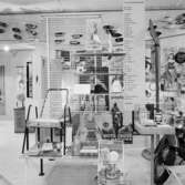 Utställning Tiotusen år. Utställningsdelen 1950-tal med trädgårdsstol och Stringhylla, Häger av trä, Bonad med textiltryck, konserver, TV- kanna och persienner från 1930-talet.