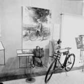 Utställning Tiotusen år. Vid Cykeln, Cykelns modell Nordstjernan 1911. Cykellykta för stearinljus. På väggen cykellykta med örn för Karbidbelysning. Byxor från Mauritz Textil smedjegatan Jönköping. Buteljkorg, flaskor och packväska