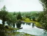 Vattendrag med en båt i förgrunden samt några mindre hus i grönskan i bakgrunden.; Idyll i Resele (Hoven)