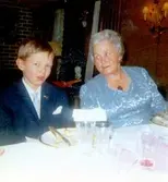 Manne Ekman (född 1955) och Elin Rotwall (1901 - 1988) sitter vid ett dukat bord i Leksandsgården 1965-12-18. Det är bröllop för storebror Ulf-Göran Ekman (född 1942) och Gunilla Lagerström (1941 - 1998). Relaterat motiv: A2891.