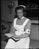 Kvinna i sjukvårdsuniform sitter i soffan och läser en bok, Östhammar, Uppland