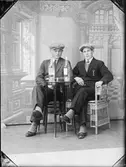 Ateljéporträtt - två unga män sitter vid ett bord med flaskor på, Östhammar, Uppland 1929