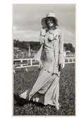 Mannekäng visar mode vid Ulriksdals galoppbana utanför Stockholm. Klänning med slätt liv, corsage vid dekolletaget. Ankellång kjol med vidd. Höftlång öppen jacka. Hatt och pärlcollier. NK:s Franska damskrädderi.
