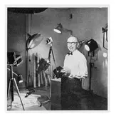 Porträtt samt artikel om Erik Holmén. Ur Nordiska Kompaniets (NK) personaltidning Rullan nummer 1, 1956. Erik Holmén var verksam som fotograf på NK. Bilderna visar dels Holmén i sin fotoateljé med kamera och annan fotoutrustning, dels fotografen som 14-årig assistent.