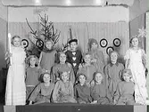 Barnen är 11 år gamla och har just uppfört ett julspel för föräldrar och släktingar, vid jul på Flickskolans teater. Lärarinna var Ruth Eriksson. Stående från vänster: Inga Svensson, Kerstin Svensson, Irene Carlsson, Birgit Roos, Mary Byfält. Mellersta raden från vänster: Gunvor Bengtsson, Birgit Lindberg, Birgit Svensson, Ulla Östlund. Längst fram, från vänster: Karin Larsson, Anne Maj Grangeus, Marianne Börjesson, Siv Christoffersson, Margret Mårtensson. (Se även bild GB2_3698)