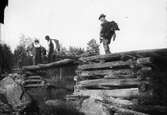  Resele cirka 1925. Fyra män som går över en enkel bro som är gjord av trä. Under bron rinner en bäck fram.