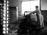 En kvinna arbetar vid varpmaskinen. Nääs fabrik i Tollered.
