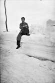 En man (heter eventuellt Ottosson) sitter avspänt utan vare sig mössa eller handskar på en hög snövall längs en väg.