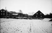 Vy över Västergården i Veddige vintertid. Bostadshus till vänster och ladugård till höger med en snöig åker i förgrunden.