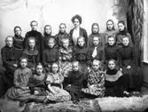 Skolfoto med flickklass och lärarinna. Modet för tiden var tydligen att antingen ha enfärgat mörk eller rutig klänning.