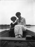 Kvinna med liten pojke sittande på aktertoften i båt. Ryd, Småland.