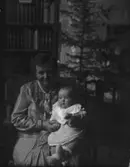 Kvinna med baby i knät framför julgran. Västerås.