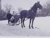 Hästekipage i snö med ett barn i släden och en kusk. Bilden tagen utmed Kungsgatan, troligen är det södra kyrkogården som syns i bakgrunden. (Se även bild MR2_1029)