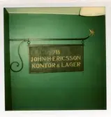 Västerås, Centrum, kv. Dominikanklostret.
Vasaparken. Kopparskylt med texten AB John E Ericsson Kontor & Lager. 1970-tal.