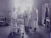 Läkare, tre sjuksystrar och flickpatient på operationssal. Man lägger om bandage om barnets fot. (Se även bild MR2_1000)