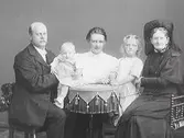 Familjebild med makar, två barn och en äldre kvinna i stort mörkt dok. (Se även bild MR2_1022)