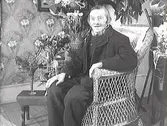 En herre som firar sin 90-åriga födelsedag sitter i en korgstol med gratulationsbuketter intill sig.Troligen en släkting till familjen Ranch.