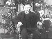 En herre som firar sin 90-åriga födelsedag sitter i en korgstol med gratulationsbuketter intill sig. Troligen en släkting till familjen Ranch. (Se även bild MR2_1313, 1314)