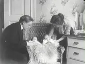 Familjebild. Föräldrar i hemmiljö med tvillingbebisar i korgstol.