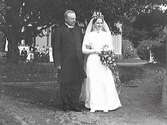 Brudparet Ernst Björck och Anna f. Holmdahl vid gårdsrundeln i trädgården. I bakgrunden ses präst och bröllopsgäster vid huset. Anna var dotter till prosten i Tvååker, Svante Julius Edvard Holmdahl och Anna Larsson-Laurell.