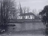 Skällinge kyrka i Halland, sedd från stranden av ett vattendrag.