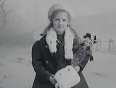 Porträtt av fotografens systerdotter Ingrid Alling med en docka. Hon är vinterklädd med pälsboa och -muff.