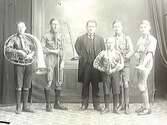 Fem pojkar med blåsinstrument i scoutliknande kläder tillsammans med en äldre man, troligen musikläraren.