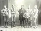 Fem pojkar med blåsinstrument i scoutliknande kläder tillsammans med en äldre man, troligen musikläraren.