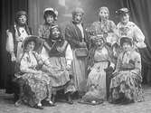 En grupp (flickor) med ansiktsmasker, utklädda till påskkärringar. Framför påskärringarna står en bur med en höna och ett ägg.
(Se även MR2_1445 där de inte bär maskerna)