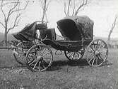 Fotografi av en gammal hästdragen passagerarvagn, en landå med sufflett, som står på tom utomhus.