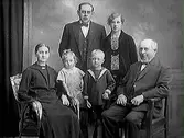 Familjebild. Familj från Träslöv. Kan möjligen vara tre generationer med det äldsta paret sittande, ett medelålders par stående och deras två barn.