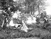 Utflykt. Delar av familjen Ranch på utflykt har slagit sig ner i en slänt vid en stengärdsgård. Ett par av männen läser i tidningar. Kvinnan till vänster med stor, svart slöja: Hulda Lindh; kvinnan näst längst till höger: Nathalia Ranch; kvinnan längst till höger Mathilda Ranch själv. (Se även MR2_667)
