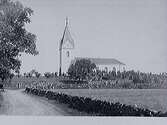 Valinge kyrka i Halland, sedd från Gödestadsvägen i söder som i korsningen möter Skolvägen. Kyrkans torn är från 1840 medan långhus och kor ritades av Fredrik Ekholm och uppfördes 1891. Vägarna kantas av stengärdsgårdar. (Se även bild MR2_557)