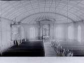 Interiörbild av Värö kyrka, vy från läktaren mot koret. Altargång, altarring, altaruppsats, predikstol, kyrkbänkar. Flackt välvt tak indelat i rutmönster. (Se även bild MR2_569)