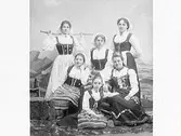 Sex personer iklädda olika folkdräkter, troligen personal och bekanta till fotografen. Sittande till höger är kollegan Elof Ernwald, övriga är flickor.