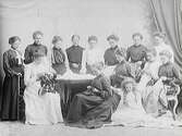 Ateljébild med en grupp kvinnor, samt en flicka, som syr. På bordet ett utbrett tygstycke. Eventuellt personal hos ett damskrädderi (Augusta Pehrsons?). Kanske reklamfoto?