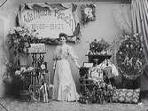 Mathilda Ranchs fotograffirma fyller 25 år 1907. Hon poserar i ateljén bland blomsteruppsättningar och andra presenter.