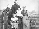 Familjebild med makar och tre barn. Fond och rekvisita ska ge en illusion av att de är vid havet.