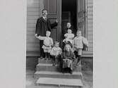 Familjebild. Ett par med fem barn samlade på en yttertrappa till ett trähus.