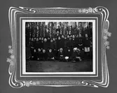 En skolklass på ett trettiotal barn med sin lärarinna ute i skogen.