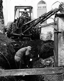 Två män, en i grävmaskin, som gräver en djup grop framför Landskyrkan.
