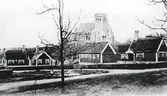 Arbetarbyn och kyrkan på Tjolöholms slott. Stugbyn var klar 1903 och samma år började kyrkan byggas. Den invigdes i oktober 1904. Anläggningen ger sken av att vara ny och det ser ut att finnas en byggnadsställning på kyrkans fasad, så troligen är bilden tagen kring 1905. Arkitekt till stugbyn var Lars Israel Wahlman och till kyrkan Hans Hedlund.